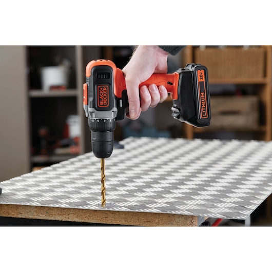 BLACK+DECKER BCD703C1 cordless drill being used to drill into a metal sheet, close-up view.