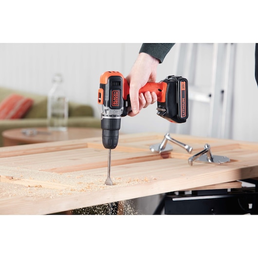 BLACKDECKER BCK21S1S cordless drill in use drilling wood, side angle, orange and black color.