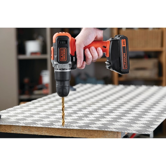 BLACK+DECKER BCK21S1S cordless drill used to drill metal sheet in workshop, close-up side angle.