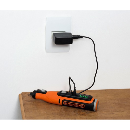 Photo of BLACK+DECKER BCRT8K35 cordless screwdriver charging with cable connected to wall outlet, tool on wooden surface.