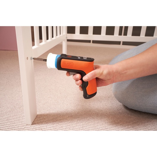 BLACKDECKER BCRTA601I orange cordless screwdriver assembling white furniture, side angle.