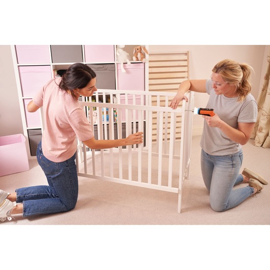 BLACKDECKER BCRTA601I cordless screwdriver in use while assembling white baby crib in a nursery room.