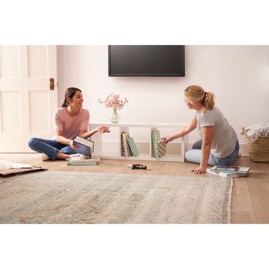 BLACKDECKER BCRTA601I cordless screwdriver on floor between two people assembling a white shelf in a living room.
