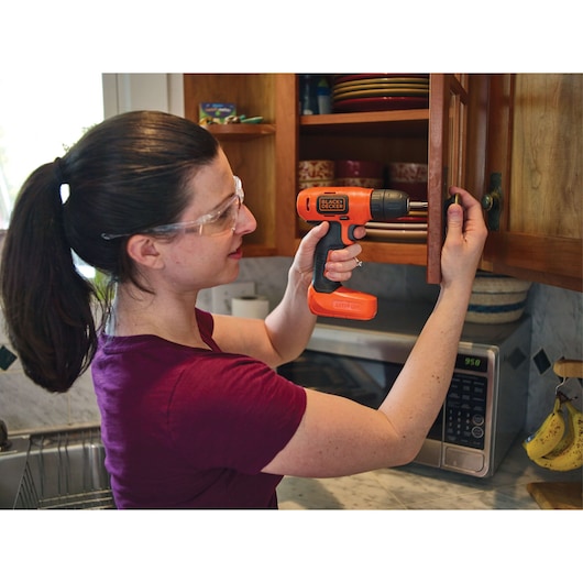 Person using BLACKDECKER BDCD8C orange cordless drill to install cabinet hardware in kitchen.