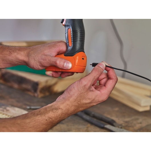 Close-up of hands plugging charging cable into BLACKDECKER BDCD8C cordless drill in workshop.