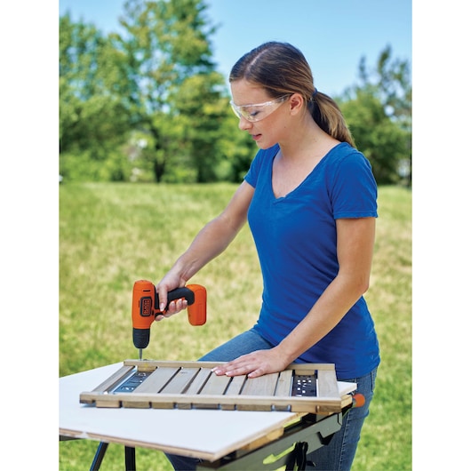 Photo of person using BLACKDECKER BDCD8C cordless drill on wooden panel outdoors.