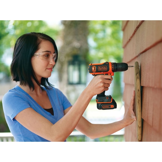 Photo of person using BLACKDECKER BDCDD12C cordless drill on an outdoor wall.