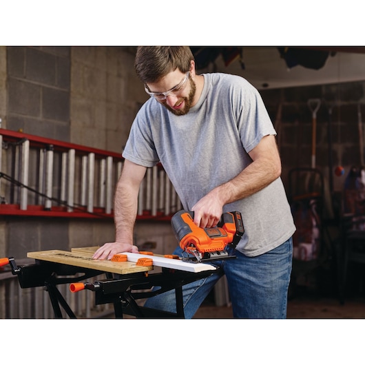 Photo of BLACKDECKER cordless jigsaw BCK22S1S in use, cutting wood on a workbench in a workshop.