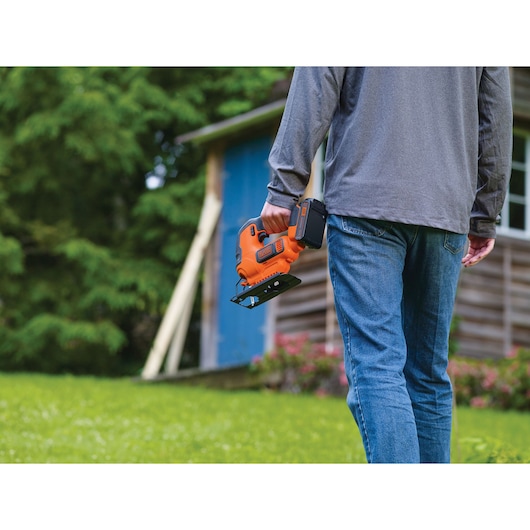 Photo of person holding BLACKDECKER cordless jigsaw BCK22S1S outdoors, close-up on tool and lower body.
