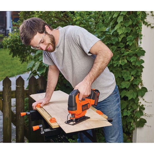Photo of a person using a BLACKDECKER BCK22S1S cordless jigsaw to cut wood on a workbench outdoors.