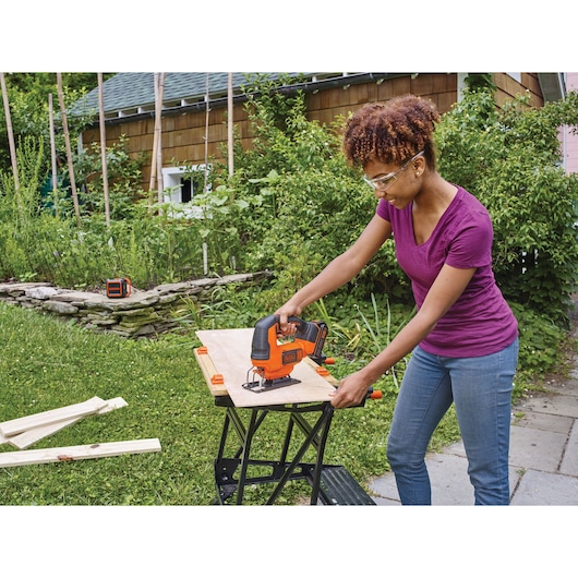Photo of BLACK+DECKER BCK22S1S cordless jigsaw in use cutting wood outdoors on a portable workbench.