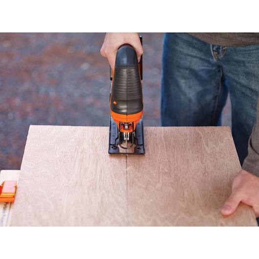 BLACKDECKER BCK22S1S jigsaw cutting along a straight line on plywood, hand gripping the top handle.