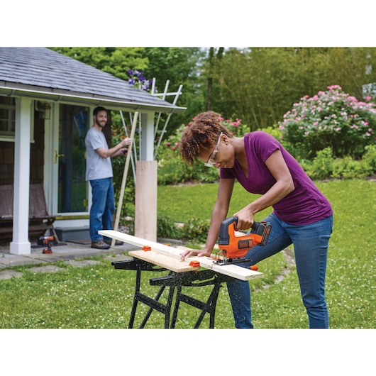 BLACKDECKER BCK22S1S jigsaw used outdoors on wood plank by person in purple shirt, garden background.