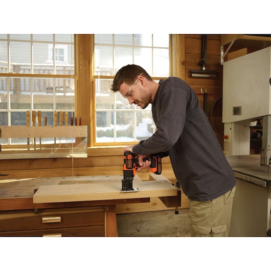 Photo of a person using BLACK+DECKER BDCMTJS jigsaw attachment on a wooden workbench in a workshop.