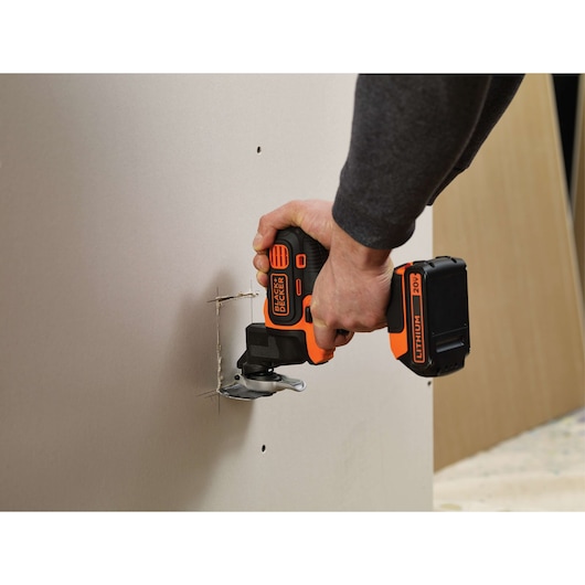 Photo of BLACKDECKER BDCMTO cordless oscillating tool cutting drywall, close-up action view.