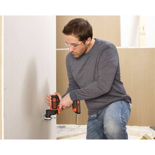 Person using BLACKDECKER BDCMTO oscillating multi-tool to cut drywall, tool features black and orange design.