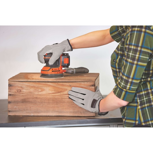 BLACKDECKER BDCRO20C sander used to sand a wooden box, operator wearing gray gloves and plaid shirt.