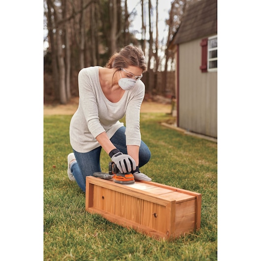 Photo of person using BLACKDECKER BDCRO20C sander on wooden drawer outdoors.