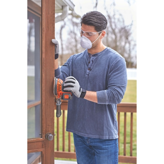 BLACKDECKER BDCRO20C cordless orange sander used on wooden door frame outdoors.