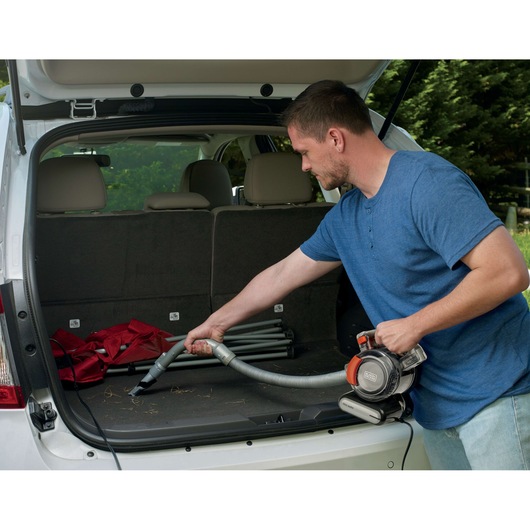 BLACKDECKER BDCV560F-LA handheld vacuum cleaning car trunk with folding chairs and debris visible.