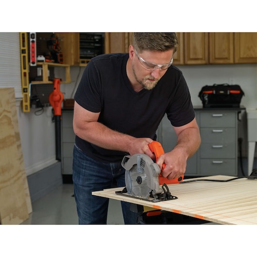 Photo of person using BLACK+DECKER circular saw BDECS300C to cut plywood in a workshop.