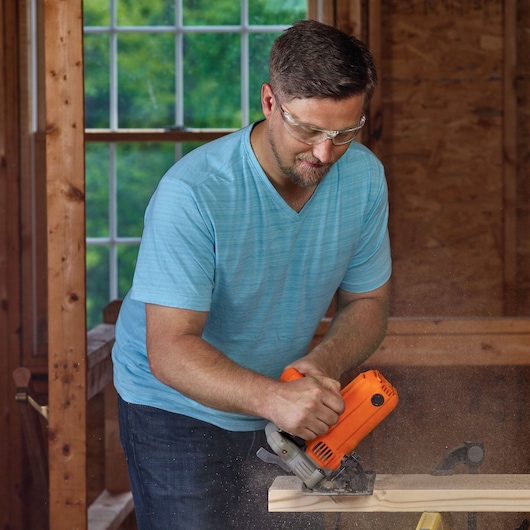 BLACKDECKER BDECS300C orange circular saw cutting wood plank, construction setting.