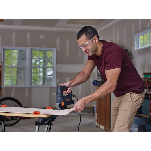 Photo of BLACKDECKER BDEJS4C jigsaw cutting wood on workbench in a garage workshop setting.