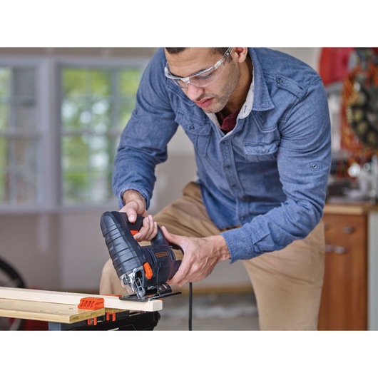 BLACKDECKER BDEJS4C jigsaw in use cutting wood, man in blue shirt and tan pants working in a workshop.