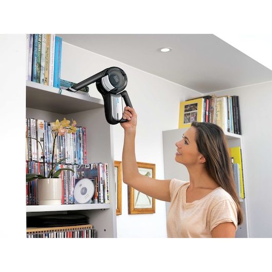 BLACKDECKER BDH2000PL handheld vacuum cleaner used to clean a high bookshelf in a living room.