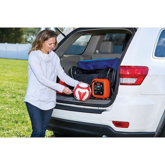 BLACKDECKER BDINF12C digital inflator in car trunk inflating a red and white soccer ball outdoors.