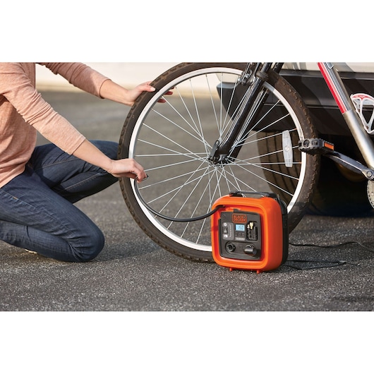 Photo of BLACK+DECKER BDINF12C inflator being used to inflate a bicycle tire outdoors.