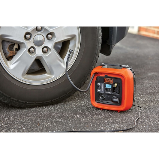 BLACK+DECKER BDINF12C portable inflator in orange, inflating a car tire on pavement, front angle.