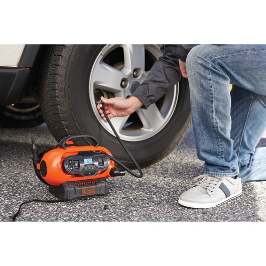 BLACKDECKER BDINF20 portable air inflator in use inflating a car tire on pavement.