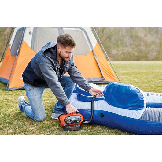 Photo of BLACKDECKER BDINF20 inflator being used outdoors to inflate a blue air mattress near an orange tent.