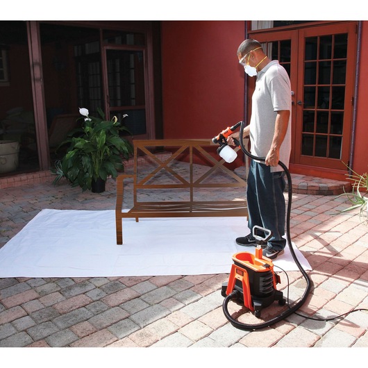 BLACKDECKER BDPH1200 paint sprayer in use, man spraying wooden bench outdoors on patio.