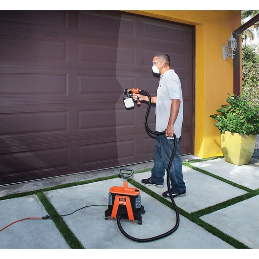 BLACKDECKER BDPH1200 paint sprayer used to paint a brown garage door outdoors.