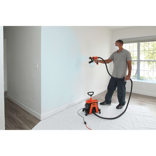 Photo of BLACKDECKER BDPH1200 paint sprayer being used to paint an indoor wall, unit on the floor with hose connected.