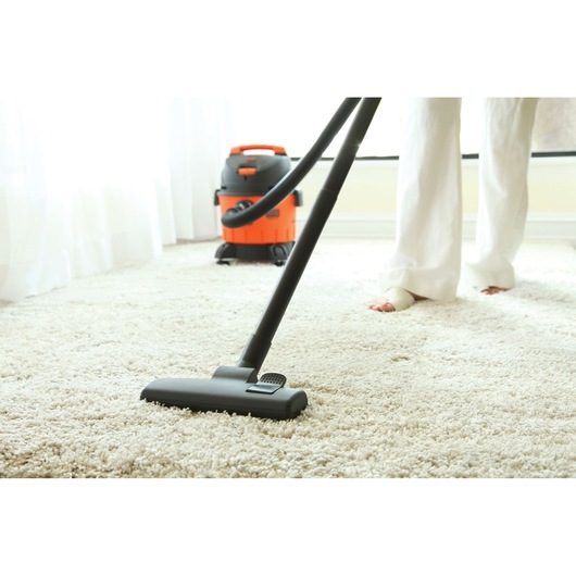 BLACKDECKER BDWD15 wet dry vacuum cleaning carpet in a bright room, photography from side angle.