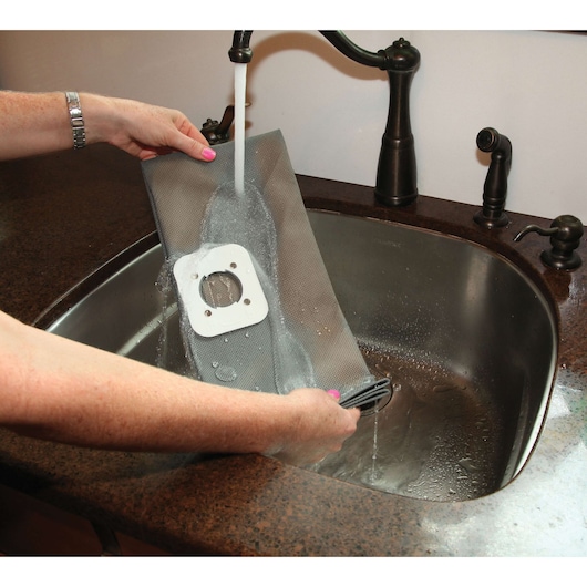 BLACKDECKER BDWD20 vacuum filter being rinsed under faucet in kitchen sink.