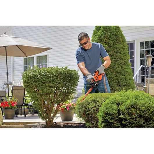 Photo of BLACKDECKER hedge trimmer BEHT150 in use trimming bushes outdoors in garden setting.