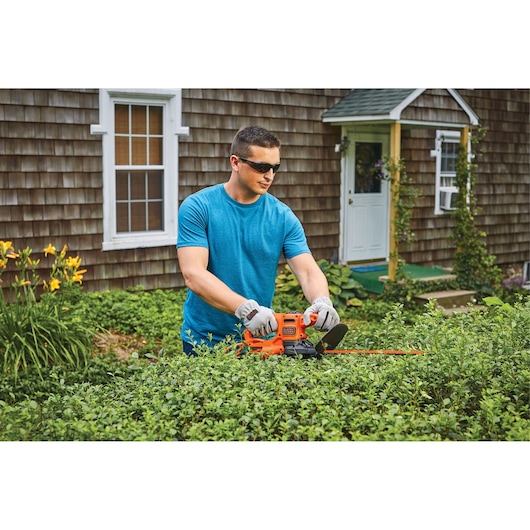 Photo of BLACKDECKER BEHT150 hedge trimmer in use trimming bushes outdoors near a house.