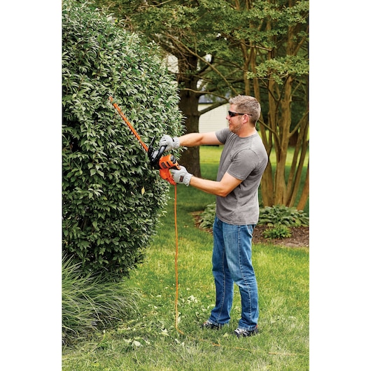 Photo of BLACKDECKER BEHT350 hedge trimmer in use outdoors, cutting a large shrub.