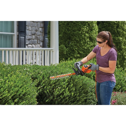 Photo of BLACKDECKER BEHT350 hedge trimmer used to trim green bushes in front of a house.