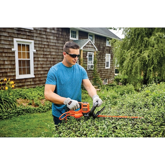 Photo of BLACKDECKER hedge trimmer BEHT350 being used outdoors to trim green bushes.