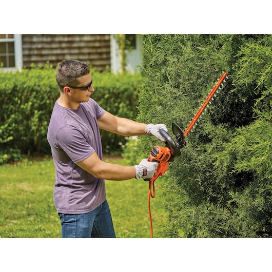 Photo of BLACKDECKER hedge trimmer BEHT350 held by person trimming green bush outdoors.