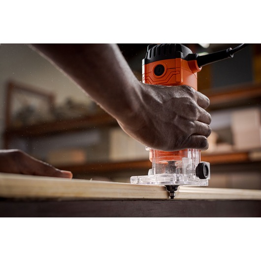 Close-up photo of BLACKDECKER BETR0500 wood router in use, hand guiding tool along the edge of a wooden board.