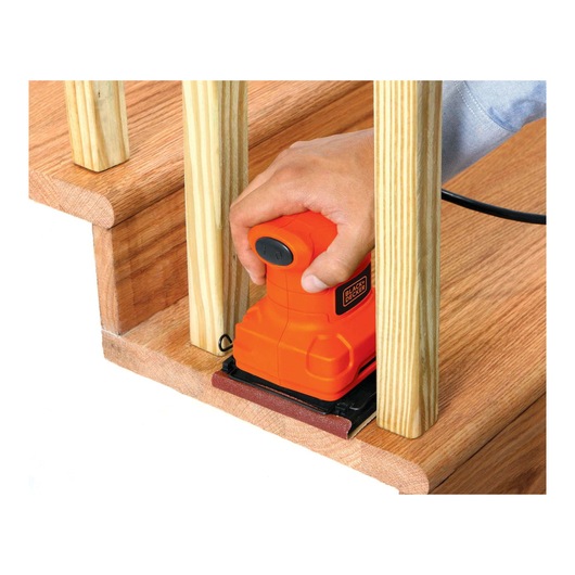 BLACKDECKER BS200 palm sander used on wooden stairs, close-up view showing orange tool and sanding work.