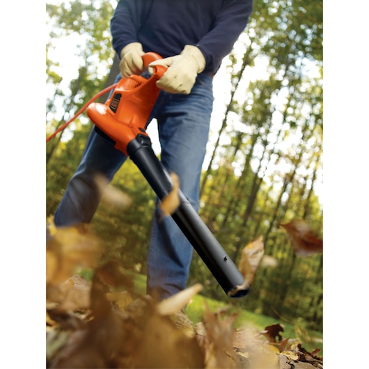 BLACKDECKER BV3600 leaf blower in use outdoors, orange body, black nozzle, scattering leaves on grass.