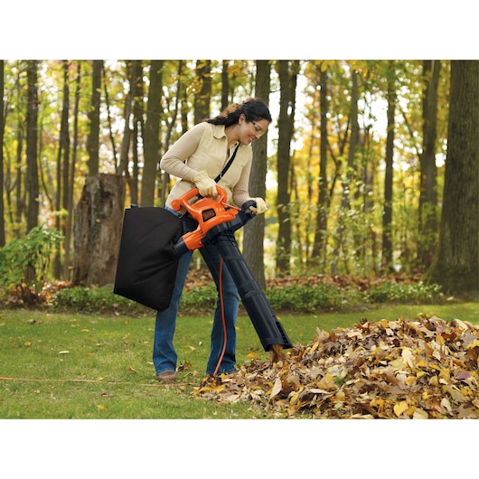 Photo of BLACKDECKER BV3600 leaf blower with vacuum attachment in outdoor use, orange and black design.