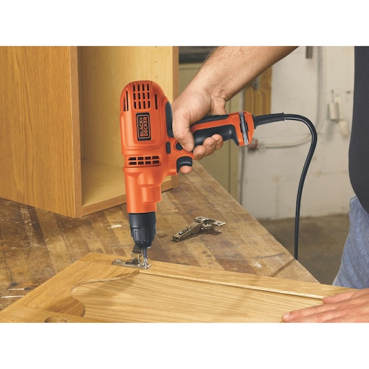 BLACKDECKER DR260C corded electric drill used to install a hinge on a cabinet door in a workshop setting.